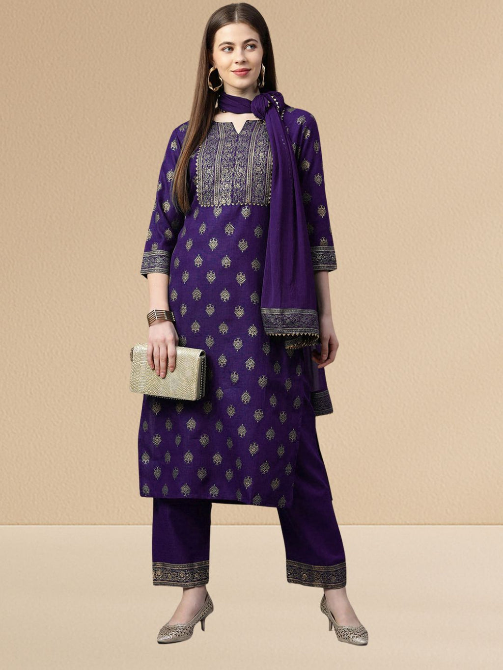 Woman wearing a deep purple cotton blend kurta set with gold embroidery on the yoke and a matching dupatta with gold lace trim.