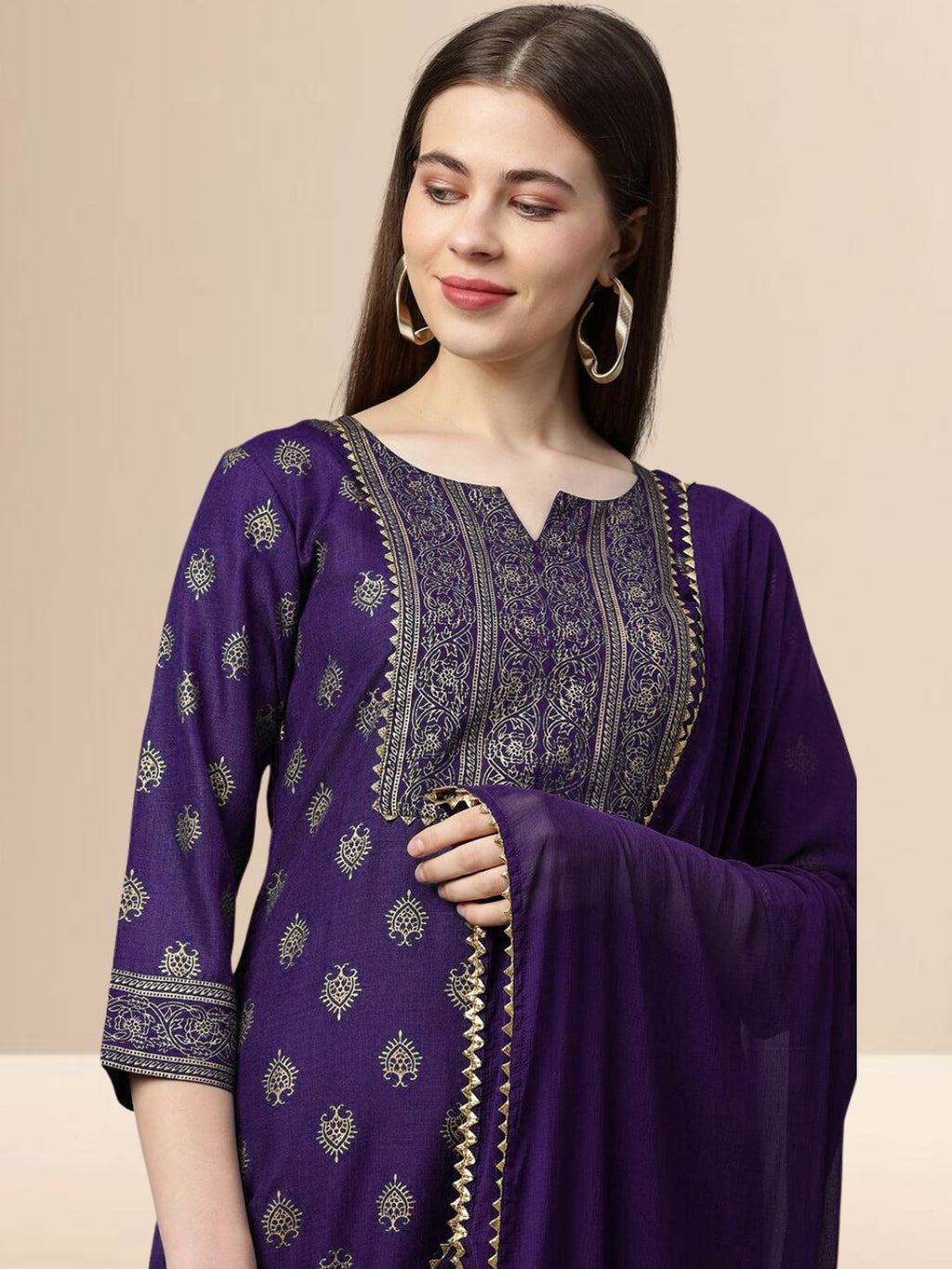 Woman wearing a deep purple cotton blend kurta set with gold embroidery on the yoke and a matching dupatta with gold lace trim.