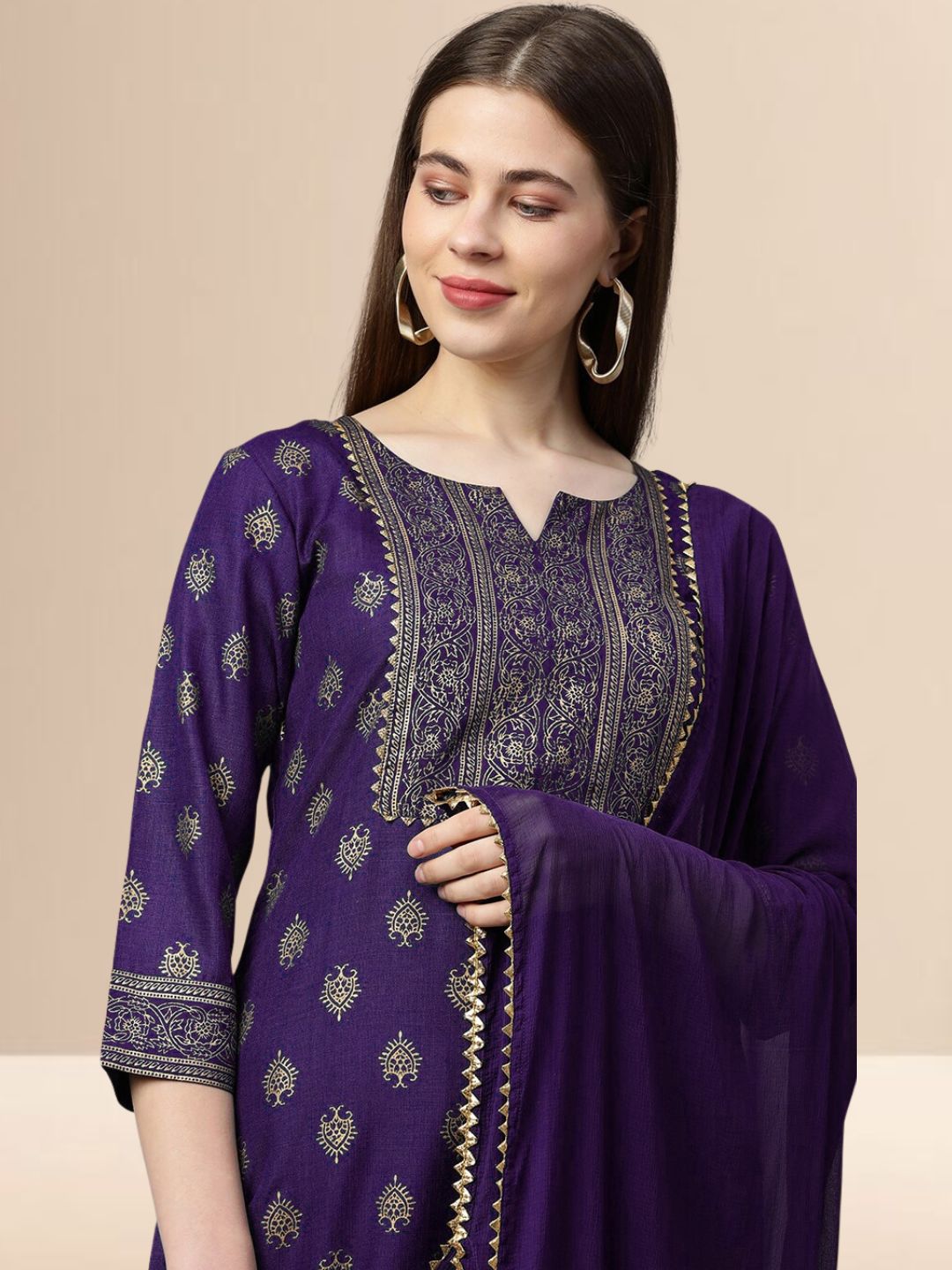 Woman wearing a deep purple cotton blend kurta set with gold embroidery on the yoke and a matching dupatta with gold lace trim.