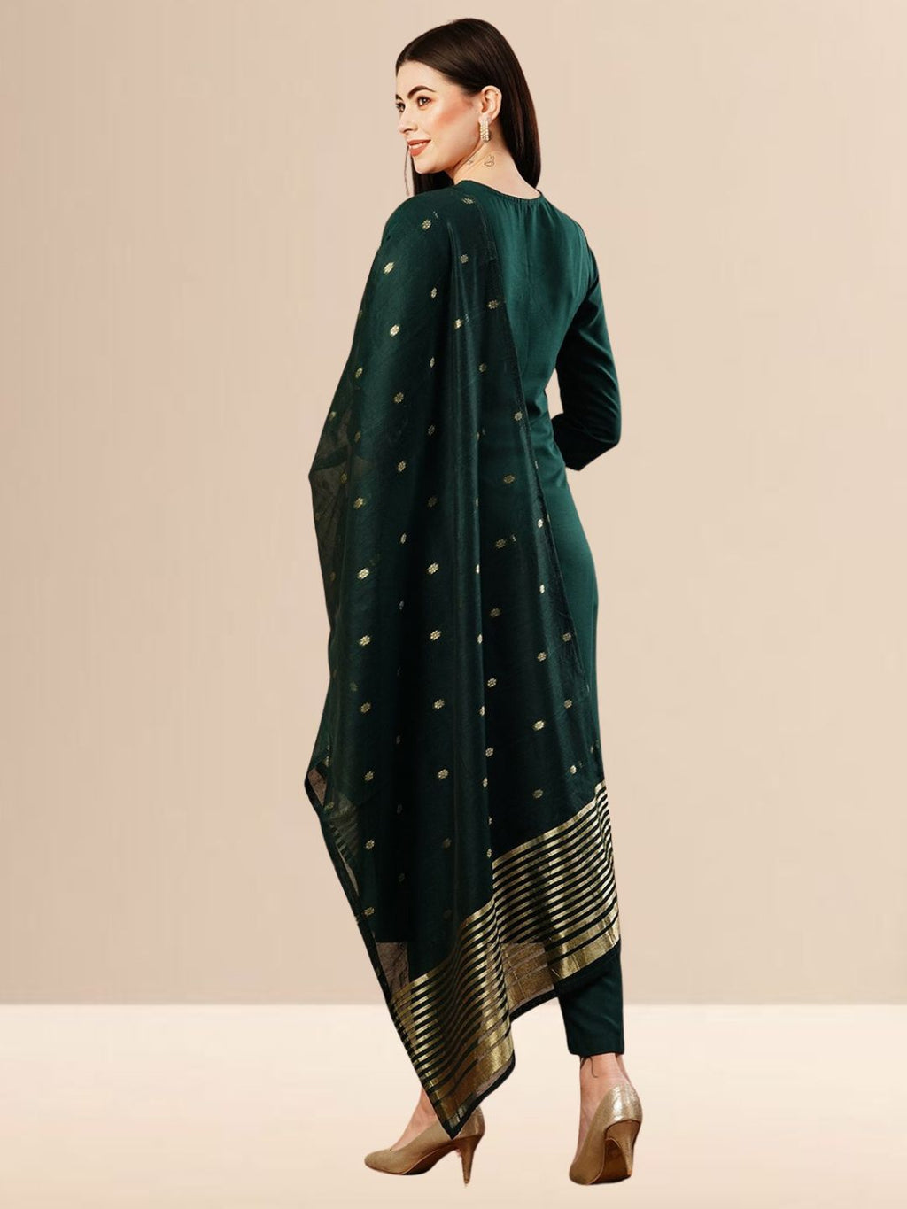 A woman wearing a deep emerald green straight-cut kurta with golden neck embroidery, black trousers, and a dark green Banarasi art silk dupatta with gold patterns.