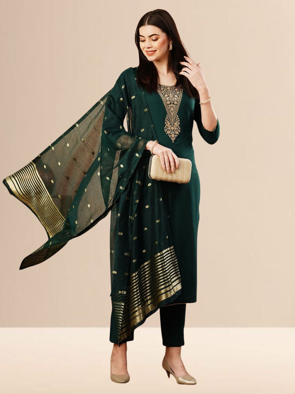 A woman wearing a deep emerald green straight-cut kurta with golden neck embroidery, black trousers, and a dark green Banarasi art silk dupatta with gold patterns.
