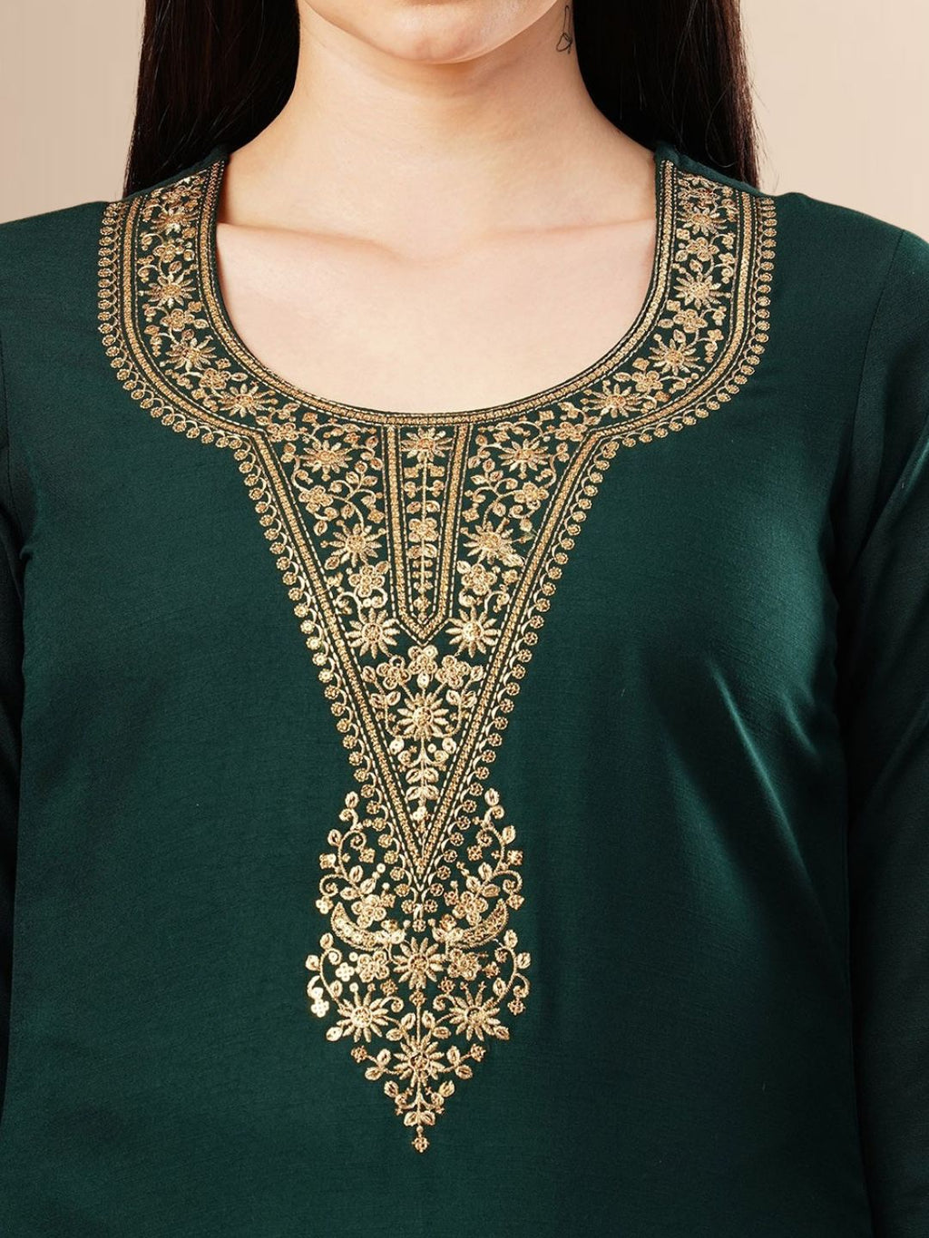 A woman wearing a deep emerald green straight-cut kurta with golden neck embroidery, black trousers, and a dark green Banarasi art silk dupatta with gold patterns.