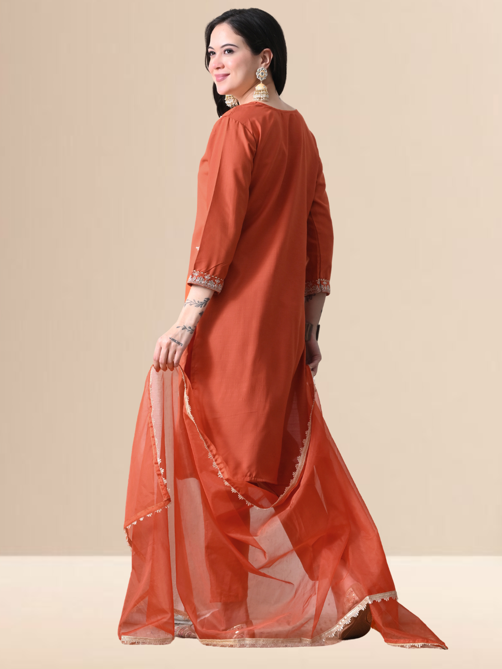 Woman wearing a rust orange Cotton  blend kurta set with silver embroidery on the neck and sleeves, paired with trousers and an organza dupatta.