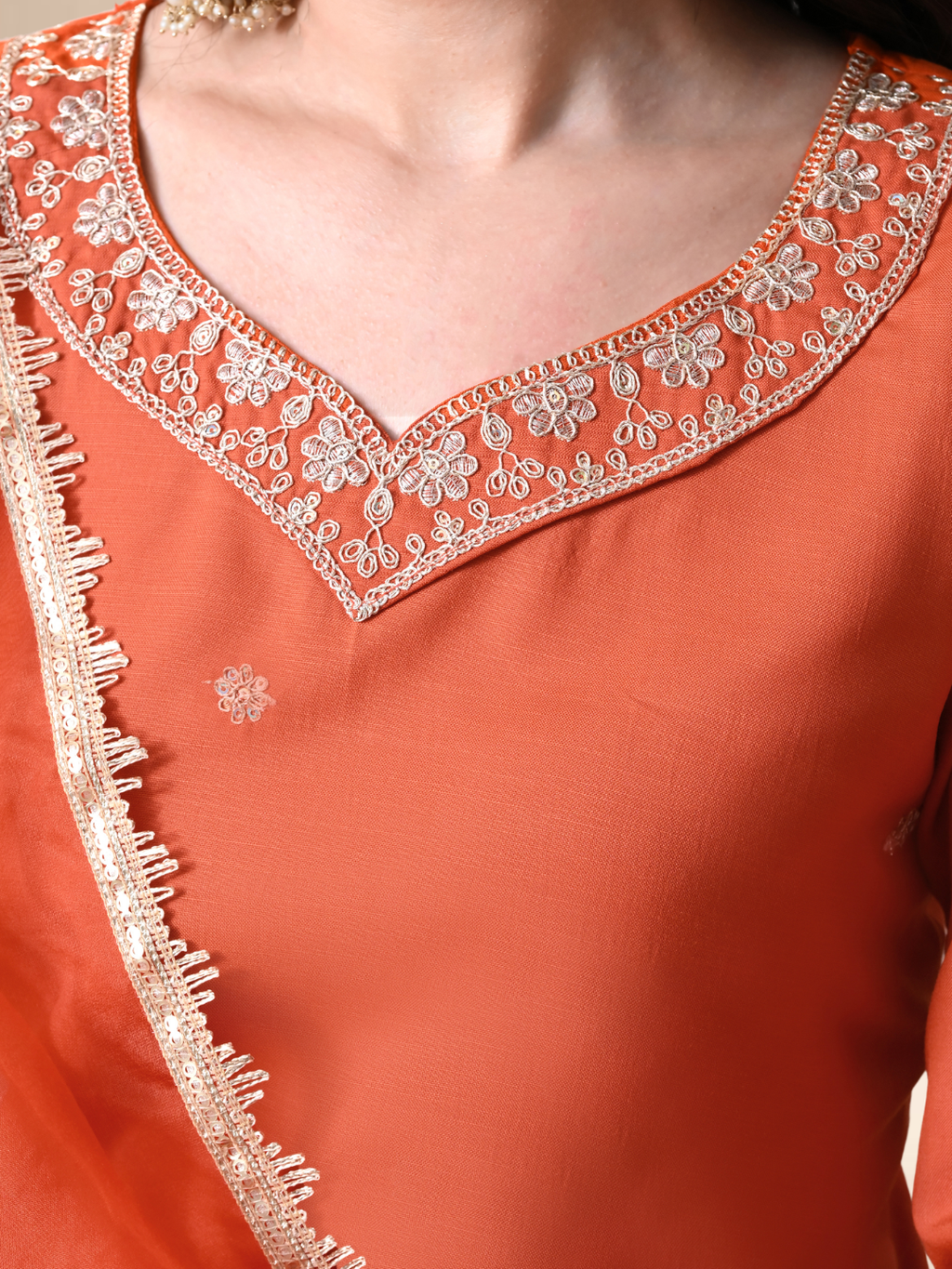 Woman wearing a rust orange Cotton blend kurta set with silver embroidery on the neck and sleeves, paired with trousers and an organza dupatta.