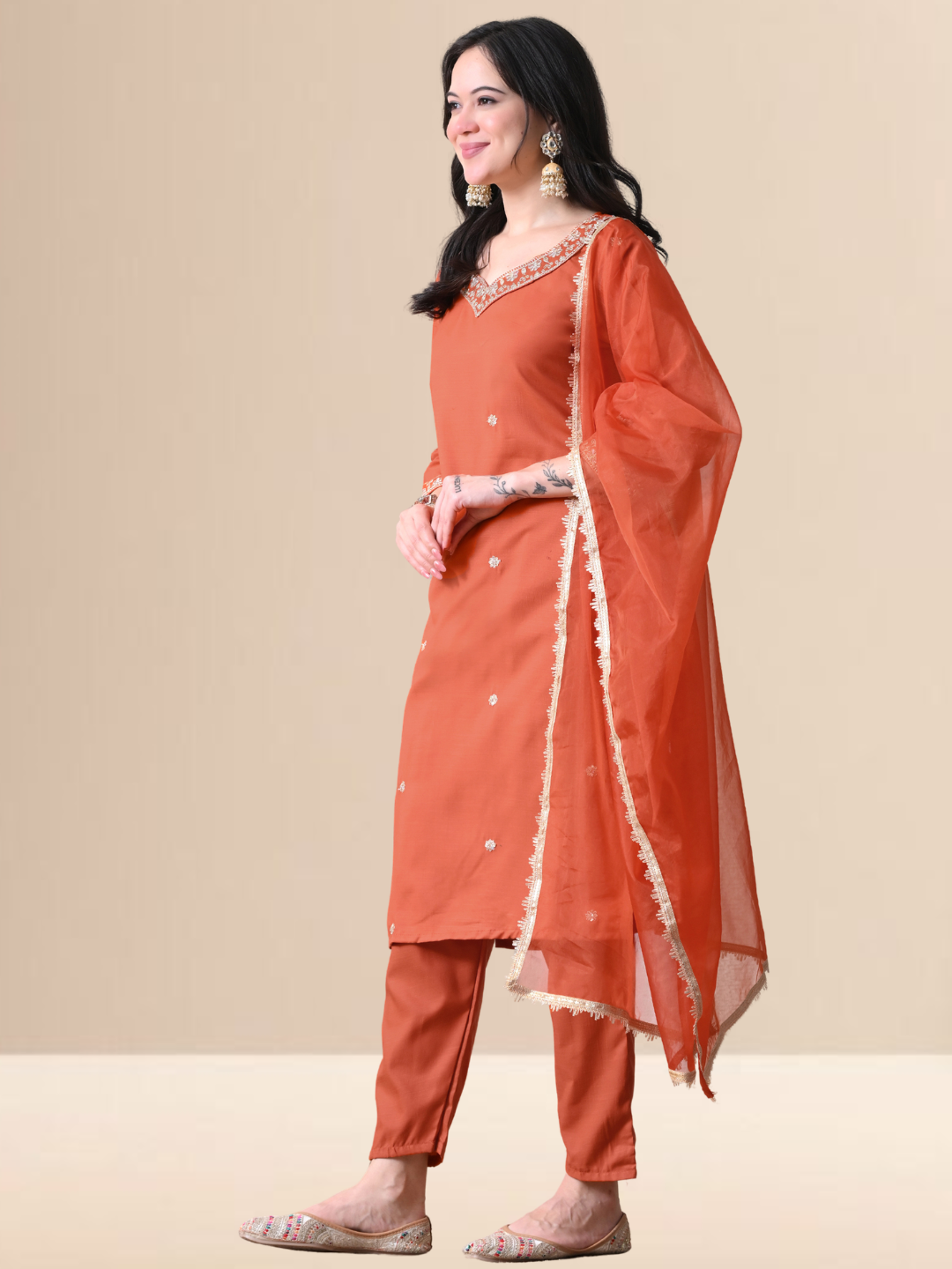 Woman wearing a rust orange Cotton blend kurta set with silver embroidery on the neck and sleeves, paired with trousers and an organza dupatta.