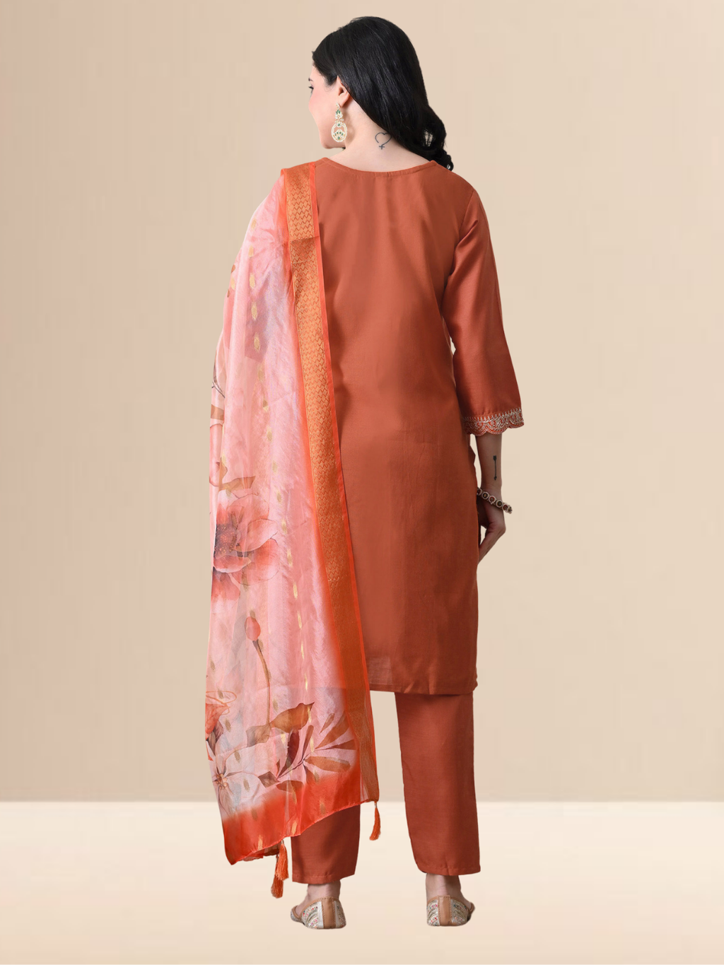 A woman wearing a rust orange straight-cut cotton blend kurta with ivory embroidery on the neck, matching pants, and a floral printed dupatta.