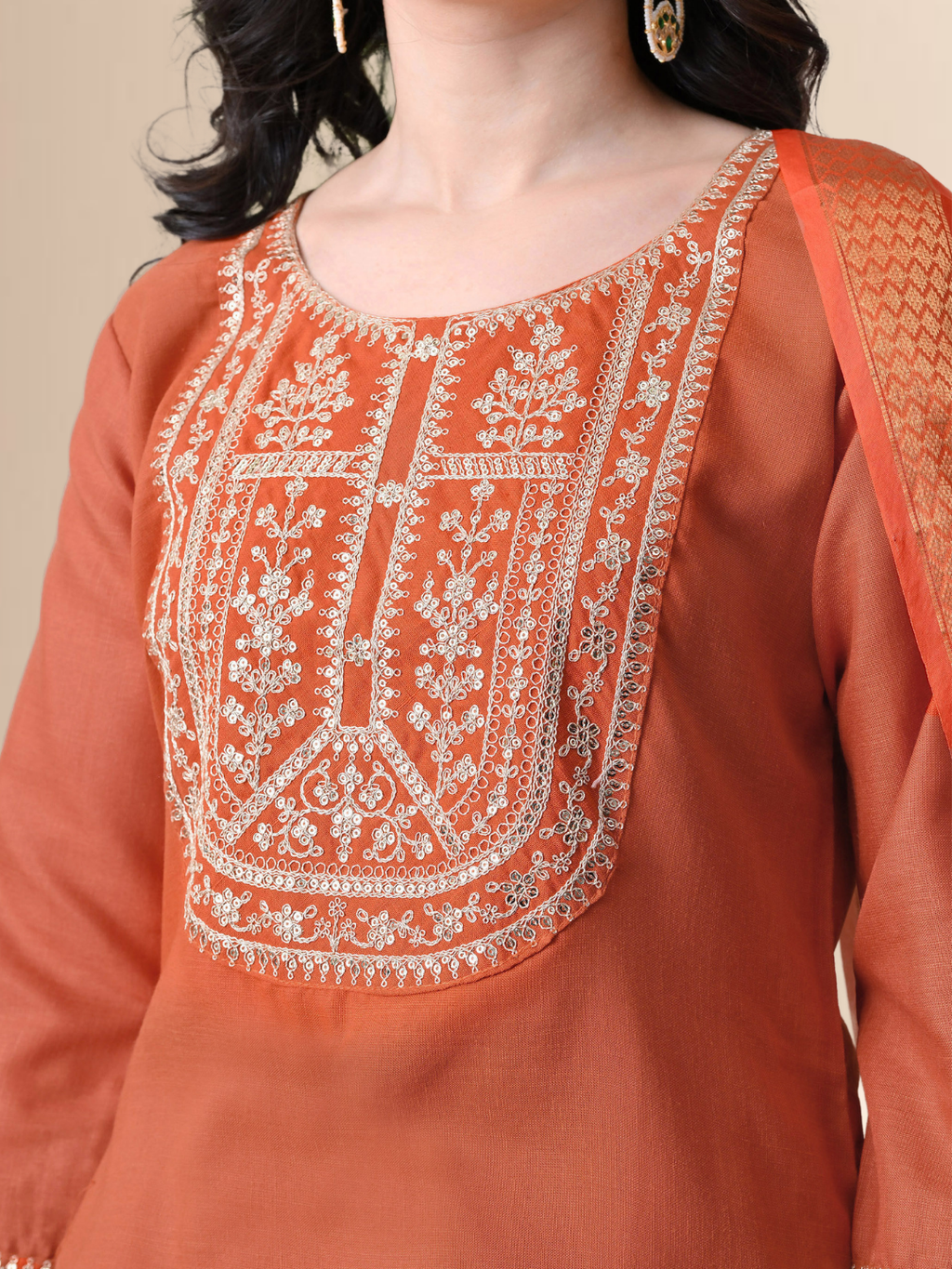 A woman wearing a rust orange straight-cut cotton blend kurta with ivory embroidery on the neck, matching pants, and a floral printed dupatta.