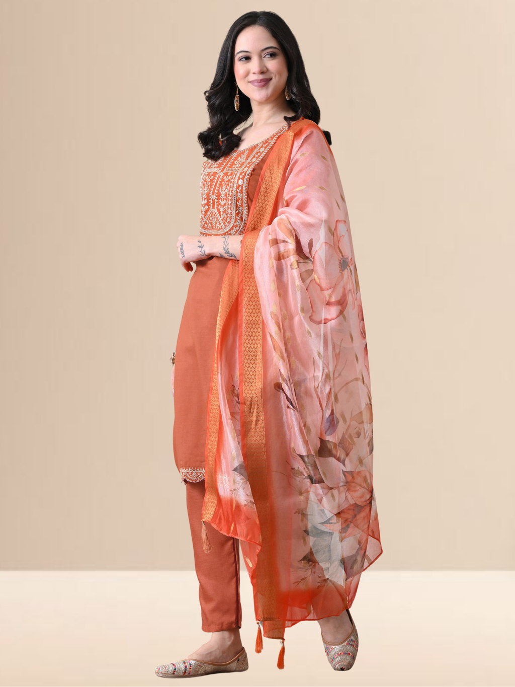 A woman wearing a rust orange straight-cut cotton blend kurta with ivory embroidery on the neck, matching pants, and a floral printed dupatta.