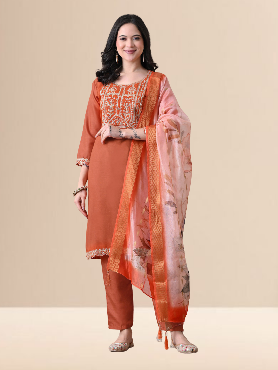 A woman wearing a rust orange straight-cut cotton blend kurta with ivory embroidery on the neck, matching pants, and a floral printed dupatta.