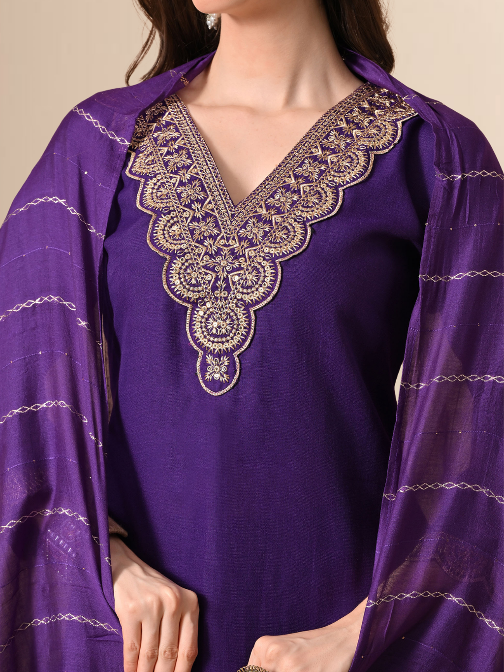 A woman wearing a royal purple straight-cut cotton blend kurta with gold V-neck embroidery, matching trousers, and a purple patterned dupatta.