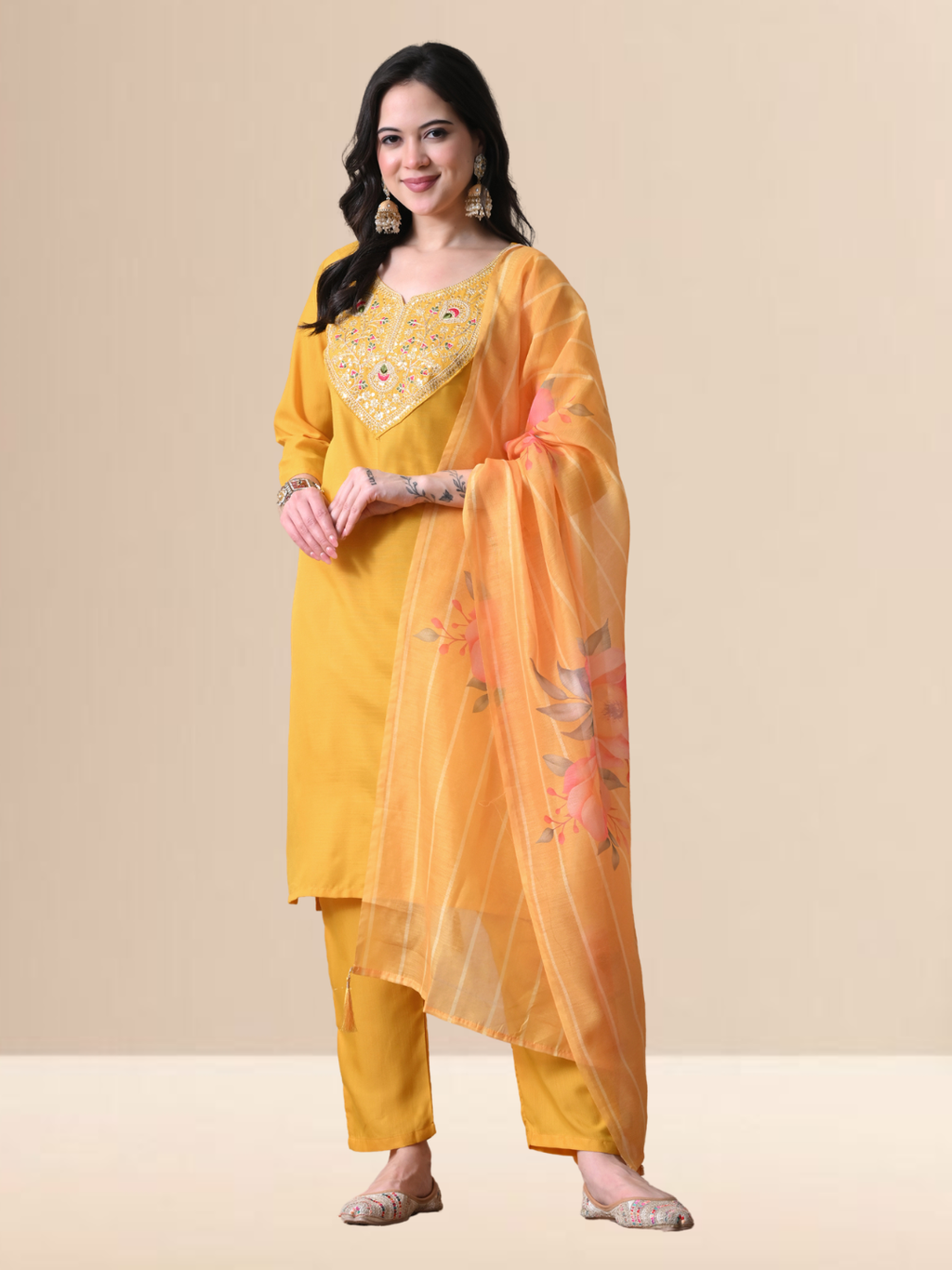 Woman wearing a mustard yellow Cotton blend kurta with multicolored floral embroidery on the neck, matching pants, and an orange floral printed dupatta.