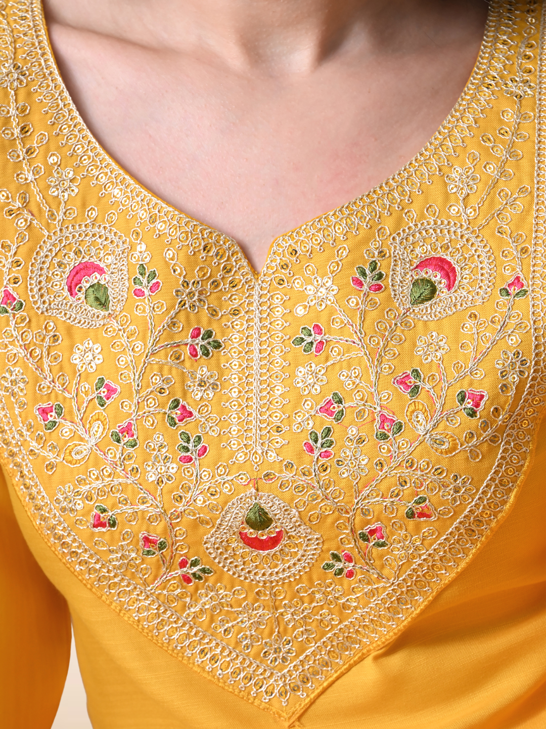Woman wearing a mustard yellow Cotton blend kurta with multicolored floral embroidery on the neck, matching pants, and an orange floral printed dupatta.