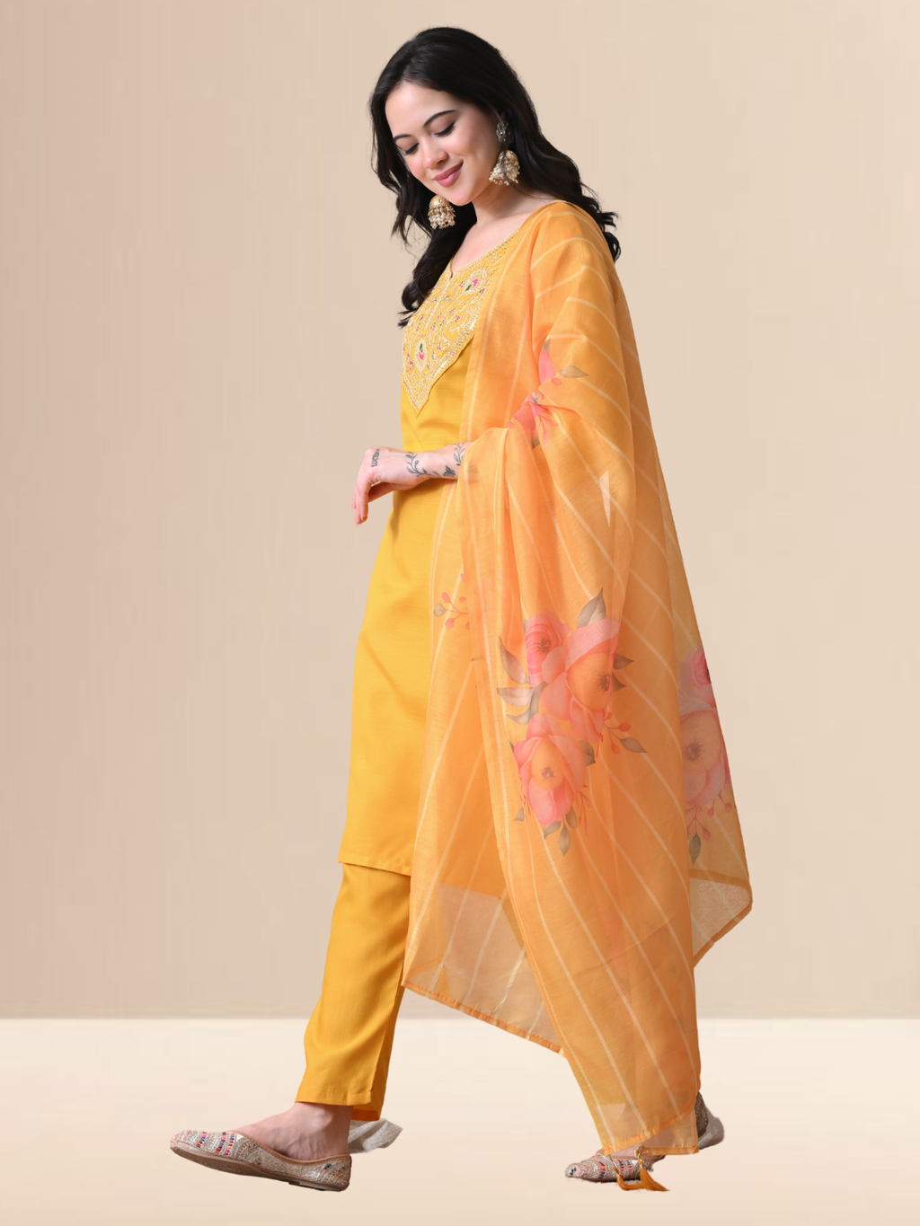 Woman wearing a mustard yellow Cotton blend kurta with multicolored floral embroidery on the neck, matching pants, and an orange floral printed dupatta.