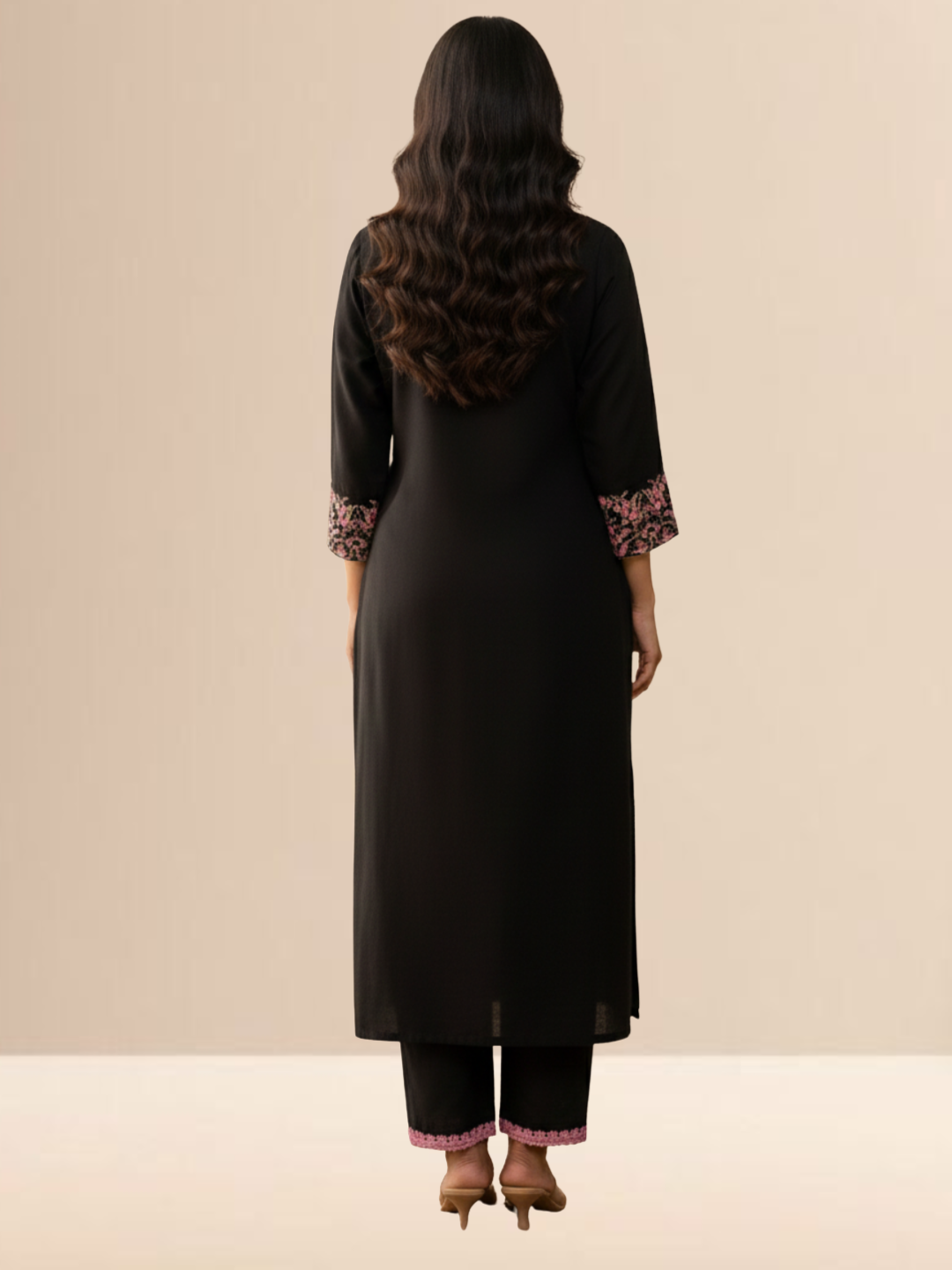 Woman wearing a jet black cotton kurta set with pink floral embroidery on the sleeves and matching lace detailing on the neckline and pants.