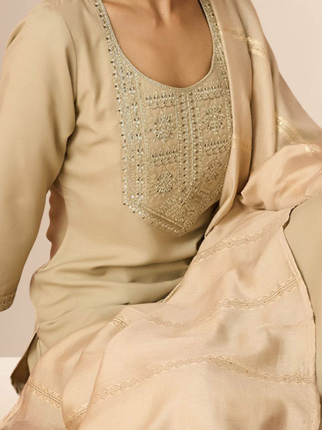 A woman wearing a beige cotton blend kurta set with an embroidered yoke, matching trousers, and a gold-bordered dupatta.