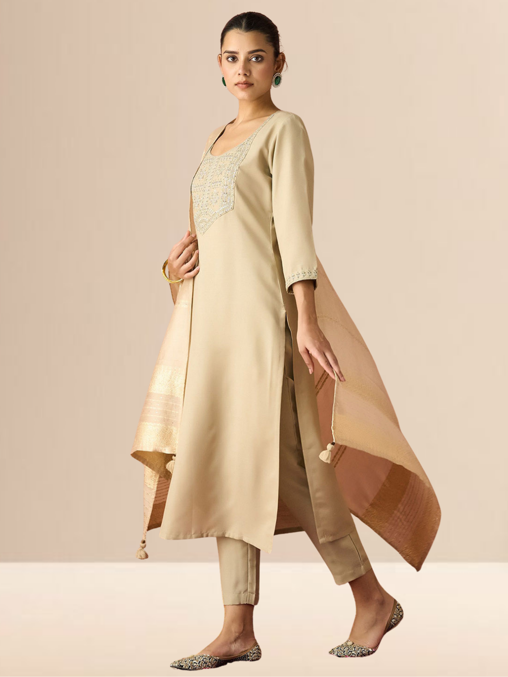 A woman wearing a beige cotton blend kurta set with an embroidered yoke, matching trousers, and a gold-bordered dupatta.