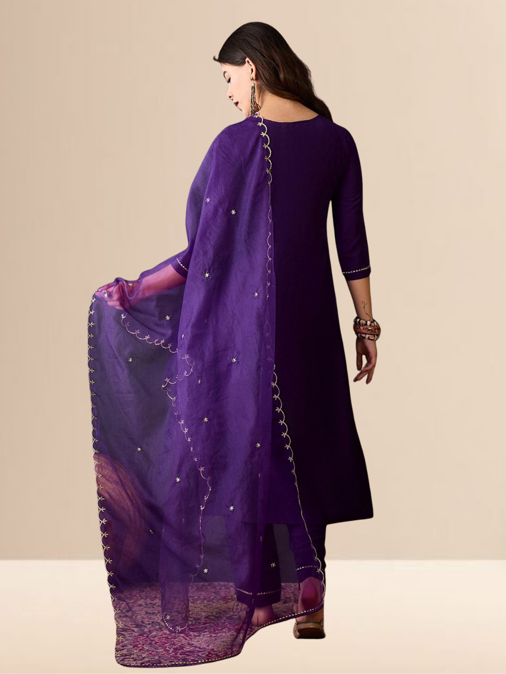 Woman wearing a purple traditional outfit with a matching dupatta on a beige background