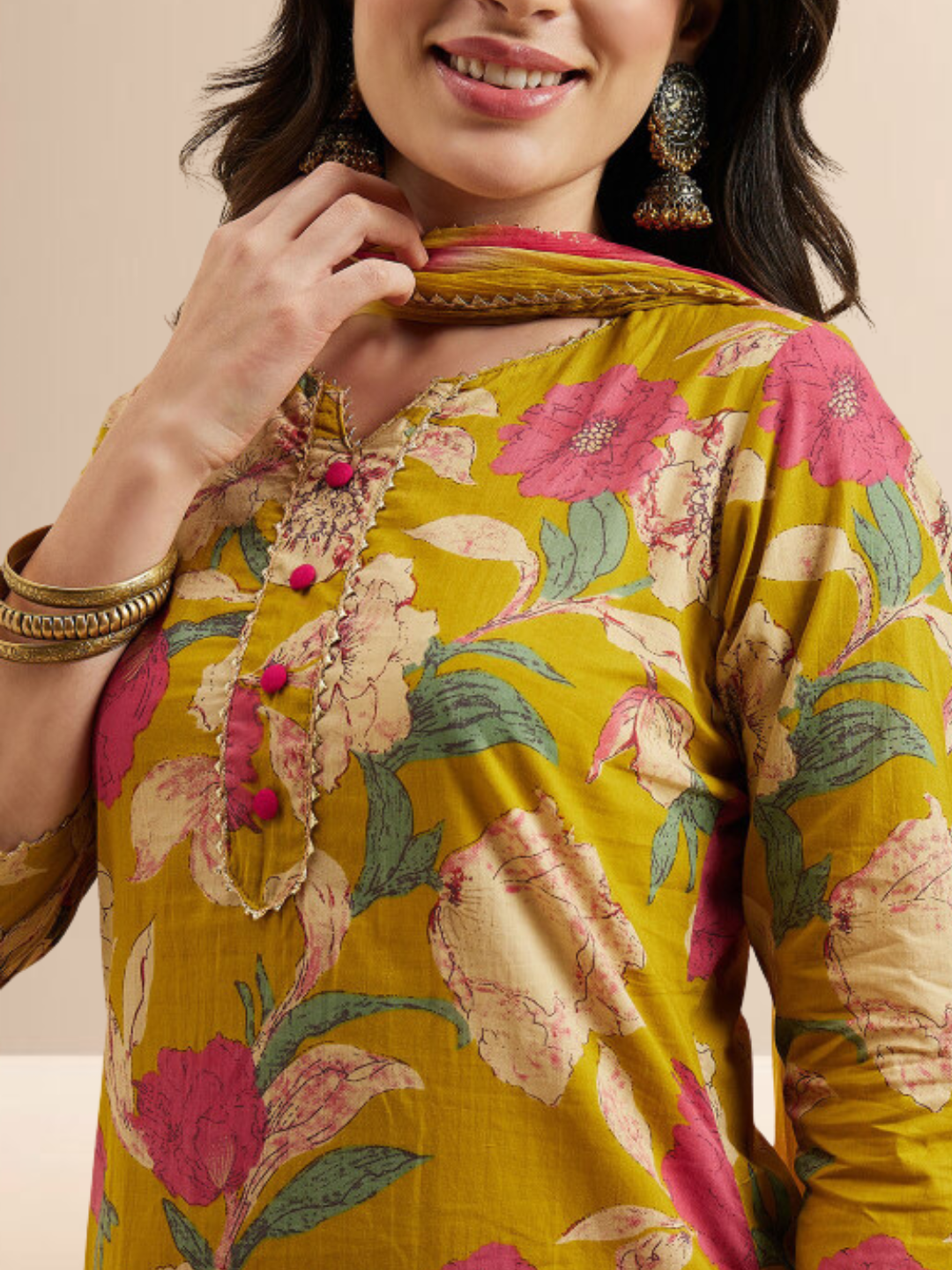 Woman wearing a mustard yellow floral printed kurta with pink pants and a yellow-pink tie-dye dupatta.