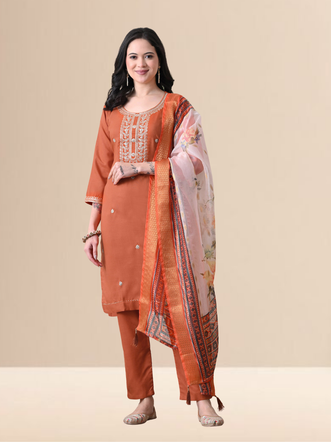 A woman wearing a rust-colored embroidered cotton blend kurta set with matching trousers and a colorful floral printed dupatta.