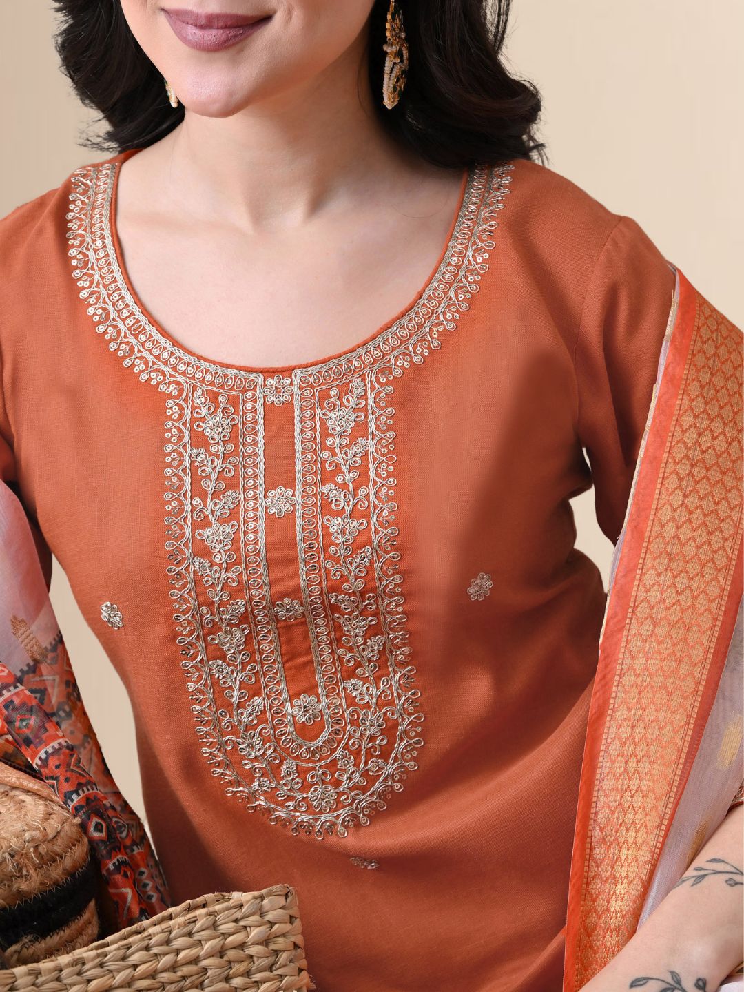 A woman wearing a rust-colored cotton kurta set with white yoke embroidery, matching rust trousers, and a white floral printed dupatta from The Desi Cloth.