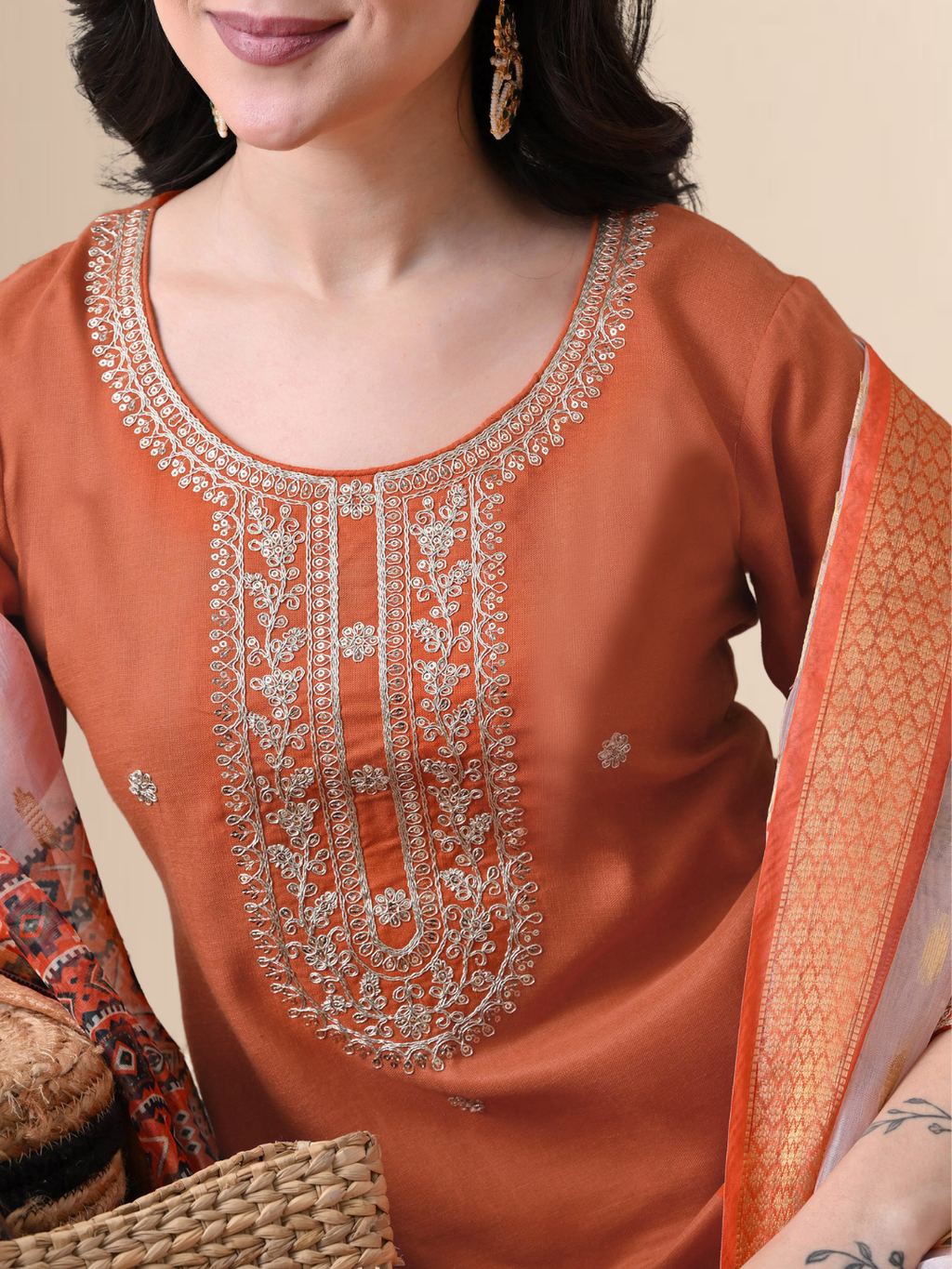 A woman wearing a rust-colored embroidered cotton blend kurta set with matching trousers and a colorful floral printed dupatta.