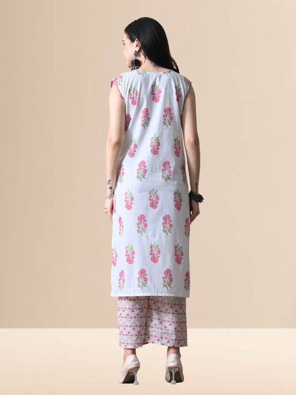 A woman wearing a white sleeveless kurta with pink floral prints and V-neck lace detail, paired with matching wide-leg floral pants from The Desi Cloth.