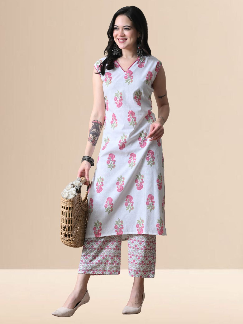 A woman wearing a white sleeveless kurta with pink floral prints and V-neck lace detail, paired with matching wide-leg floral pants from The Desi Cloth.