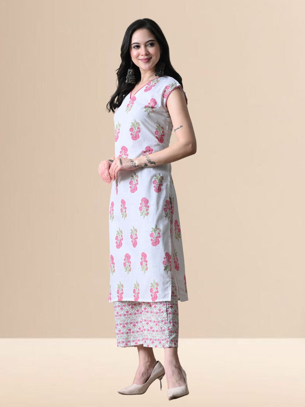 A woman wearing a white sleeveless kurta with pink floral prints and V-neck lace detail, paired with matching wide-leg floral pants from The Desi Cloth.