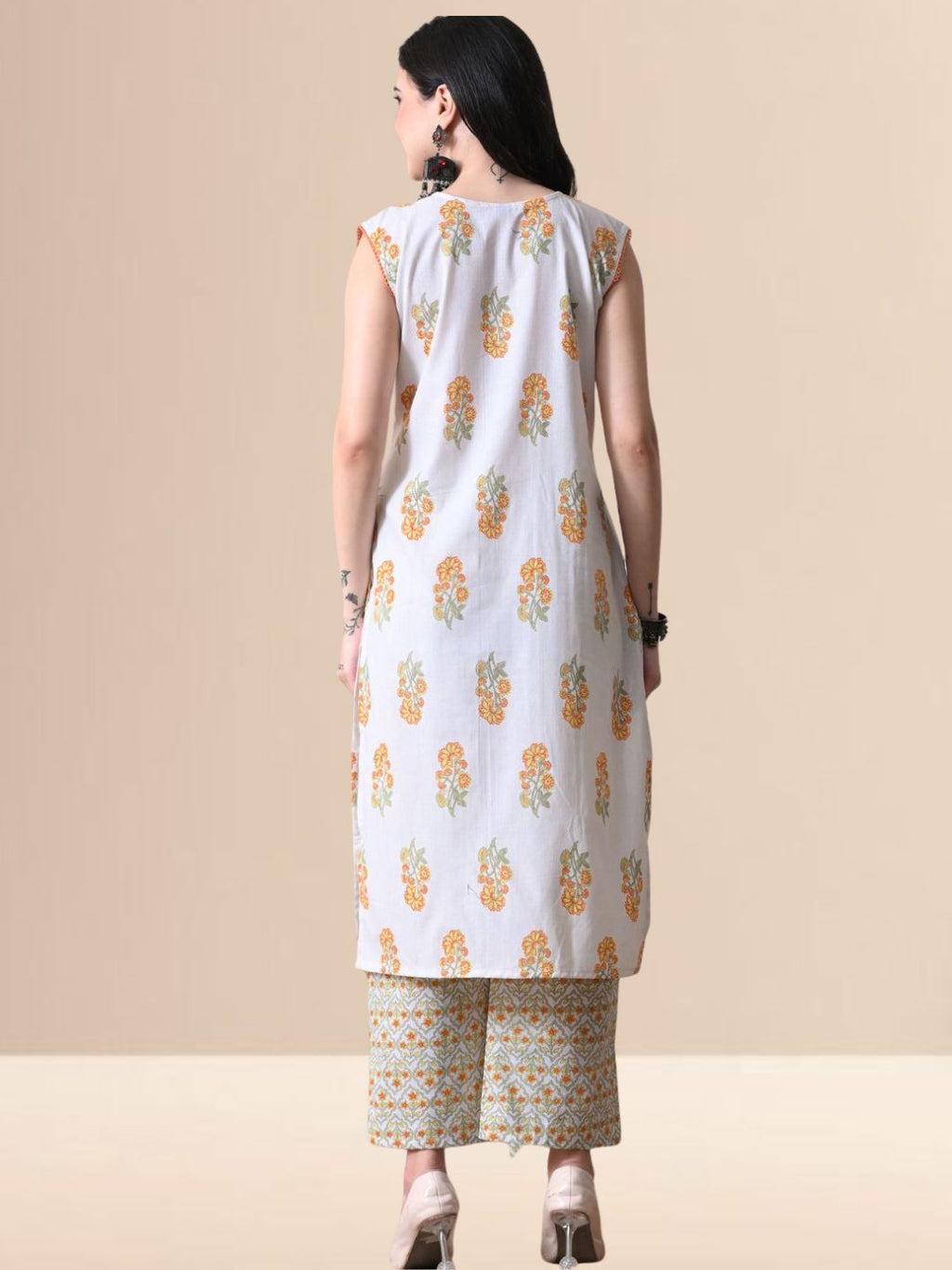 A woman wearing a sleeveless white cotton kurta with yellow and orange floral prints and a lace-trimmed V-neck, paired with matching printed wide-leg pants from The Desi Cloth.