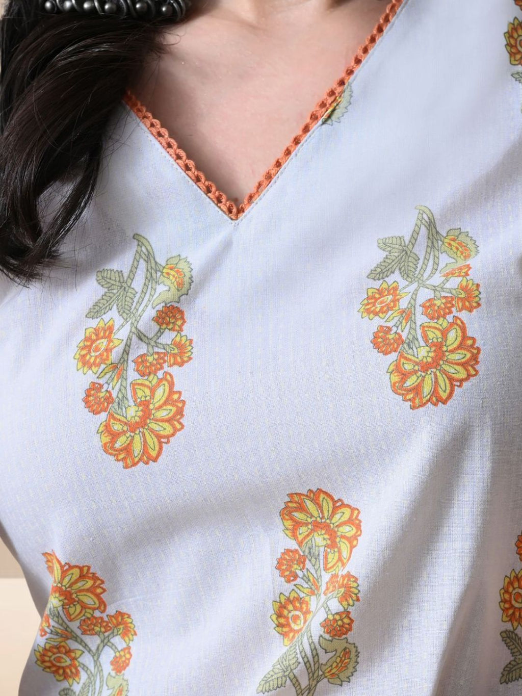 A woman wearing a sleeveless white cotton kurta with yellow and orange floral prints and a lace-trimmed V-neck, paired with matching printed wide-leg pants from The Desi Cloth.