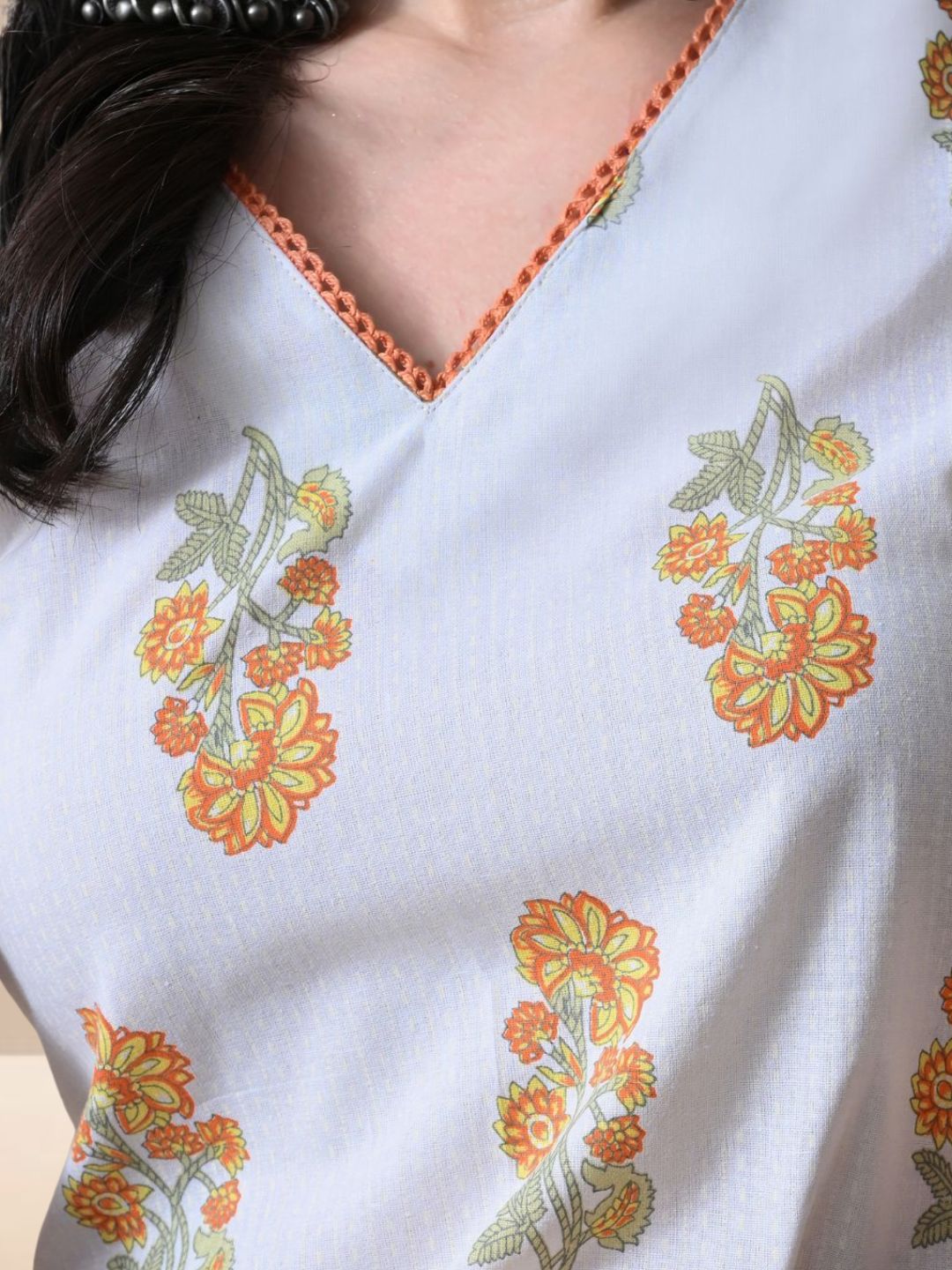 A woman wearing a sleeveless white cotton kurta with yellow and orange floral prints and a lace-trimmed V-neck, paired with matching printed wide-leg pants from The Desi Cloth.